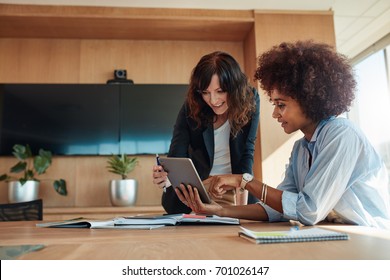 African businesswoman showing something on digital tablet to her female colleague while sitting at her desk. Professional employees discussing ideas of project on tablet pc. - Powered by Shutterstock