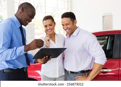 African Car Dealer Explaining Sales Contract To Couple Buying A Car