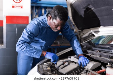 African car mechanic with screwdriver repairing car engine under the hood in auto service