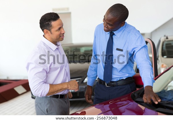 african car salesman selling a car to mid age\
customer in showroom