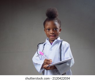 African career girl child in laboratory gown, writing in a notepad and with a stethoscope, acting like medical practitioners such as doctor, nurse or caregiver to show the benefit of science