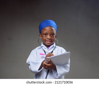 African Career Girl Child In Laboratory Gown, Writing In A Notepad And With A Stethoscope, Acting Like Medical Practitioners Such As Doctor, Nurse Or Caregiver To Show The Benefit Of Science