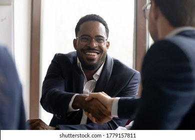 African Caucasian businessmen in formal suits express respect shake hands start negotiations. Common project growth sales increase, partnership, business etiquette, leadership, racial equality concept