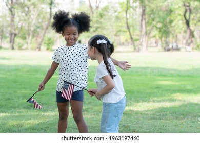 African and Caucasian kids playing together and holding small America flag at green park. Ethnic diversity of relationship with little girls at 4th of July concept - Powered by Shutterstock