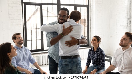 African and Caucasian millennial men embracing during group counselling therapy session. Multi ethnic people gather together provide each other psychological help, overcome problems addiction concept