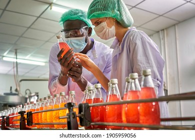 African and Caucasian worker factory are concentrating to check quality of red juice in automatically product line of beverage industry - Powered by Shutterstock