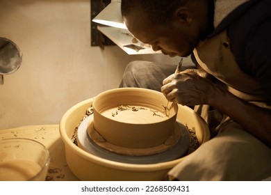 African ceramist working a bowl with a handle maker tool in a studio - Powered by Shutterstock