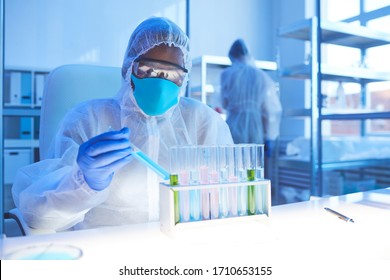 African chemist in protective workwear sitting at his workplace and working with analysis in test tubes in the lab