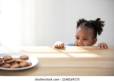 African Child Girl Hiding And Looking Chocolate Cookies Or Biscuits On Dish From Under The Table