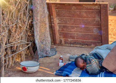 african child toddler sick with malaria medicine in the background, laying down on a blanket in the yard - Shutterstock ID 1777245836