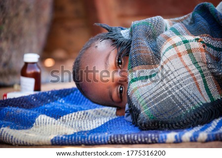 african child toddler sick with malaria medicine in the background, laying down on a blanket in the yard