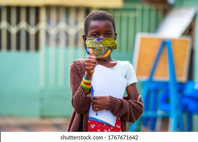 An African Child Wearing Homemade Mask For Protection And Giving A Thumbs-up At School Background - Concept On Students In Face Masks Back To School In Covid-19 Pandemic Season