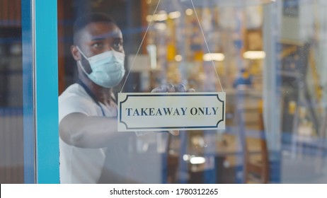 African coffee shop owner in medical mask and gloves hanging take away only sign on front door. Young afro entrepreneur opening cafe only for take away orders. Small business during quarantine concept - Powered by Shutterstock