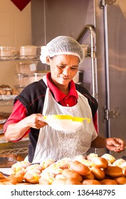 african colored woman sifting custard donuts at work in her hairnet and plastic apron