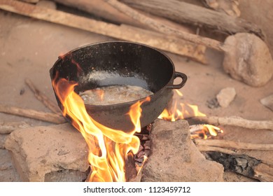 african cooking during ramadan - close up of a big black iron pot with hot oil inside, cooked outdoors over real hot fire flames on the sandy background, in the Gambia, Africa on a sunny day 
