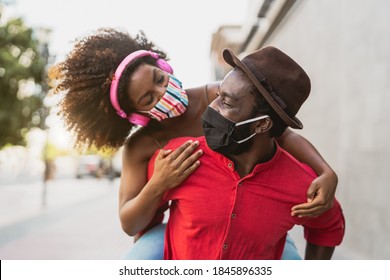 African couple piggyback wearing face mask - Happy Afro people having fun outdoor - Health care and youth relationship concept 