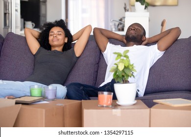 African Couple Put Hands Behind Head Rest On Sofa With Closed Eyes Big Boxes With Stuff, Breath Fresh Air Take Break On Moving Day Into New First Home. Property Buyers Or Easy Delivery Service Concept