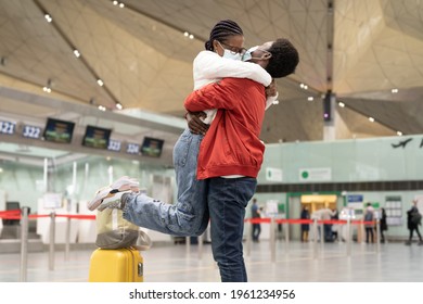 African Couple Reunion Under Covid-19 New Normality. Cheerful Man And Woman In Medical Masks Hug In Airport After Separation Due To Coronavirus Lockdown. Black Male Give Welcome Embrace To Happy Woman