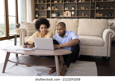 African couple sit in living room discuss receipts, control family budget, calculate household bills to pay, utility expenses, make payment via e-bank app on laptop, accounting, money control concept - Powered by Shutterstock