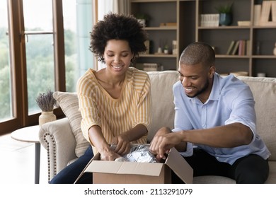 African Couple Unpack Parcel Sit On Sofa At Home, Open Box Unwrap Ordered Bough Goods Online, Get Gift From Family Living Abroad Use International Mail E-services. Delivery Services, Shopping Concept