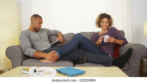 African Couple Using Electronic Devices On Couch