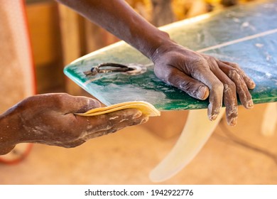 An African Craftsman surfboard Shaper working in a repair workshop with Sandpaper - Powered by Shutterstock