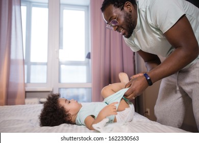 African dad changing his daughter's diaper in the bedroom