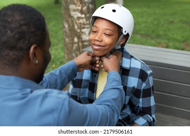 African Dad Helping His Son To Putting On The Helmet Before Game While He Sitting On Bench In Park