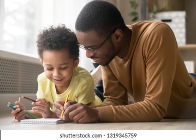 African Dad And Little Creative Toddler Kid Son Draw With Colored Pencils Lying On Warm Floor Together, Black Father Baby Sitter Teaching Help Child Boy Learning Playing At Home, Babysitting Concept