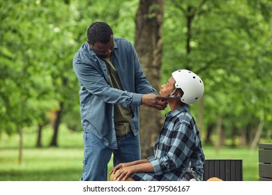 African Dad Putting Helmet On His Son Before Game While They Sitting On Bench Outdoors