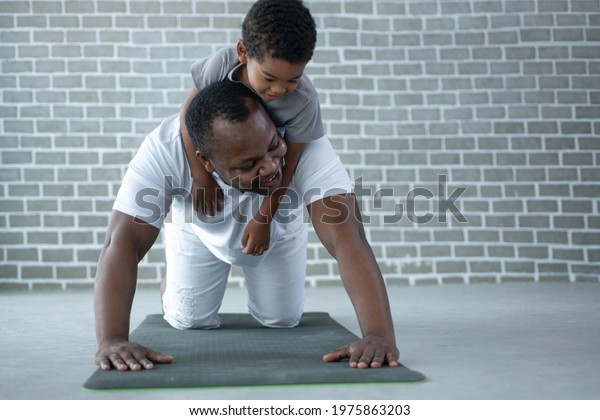 African dad and\
son exercise on floor at home, man pushup from the floor with the\
boy on his back, father\'s\
day