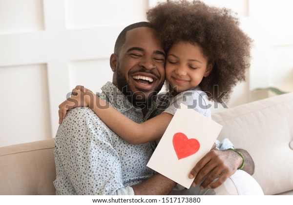 African daddy on Father Day received from caring\
little daughter paper postcard written message best wishes, drawn\
red heart as symbol of love and deep affection, family holidays\
celebration concept