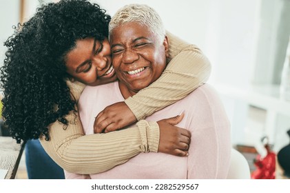 African daughter hugging her mum indoors at home - Main focus on senior mother face - Mom day and family love concept - Shutterstock ID 2282529567