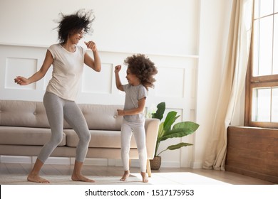 African Daughter And Mother Dancing In Modern Cozy Sunny Living Room, Babysitter And Little Kid Enjoy Summer Day At Home, Family Celebrating Vacation, Leisure, Funny Mood, Happy Active People Concept