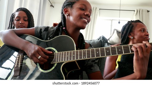 African daughter playing guitar together with family at home sofa