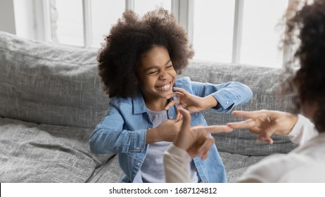 African deaf kid girl and her mother sitting on couch showing symbols with hands using visual-manual gestures enjoy communication at home. Hearing loss disability sign language learning school concept - Shutterstock ID 1687124812