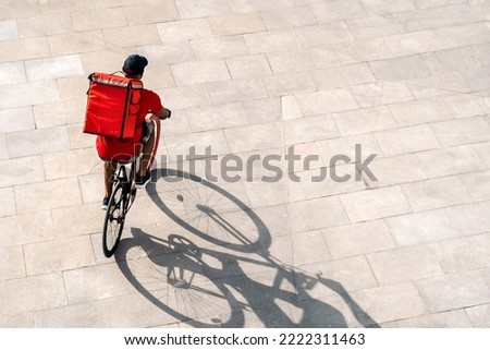 African delivery man wearing cap riding his bike in the city in his way to deliver a package.
