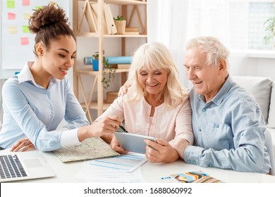 African Descent Woman Travel Agent At Office Showing Trip Itinerary To Senior Couple On Digital Tablet Smiling Cheerful