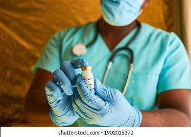 An African doctor holding a covid 19 vaccine vial in his hands while wearing blue surgical gloves and surgical scrubs