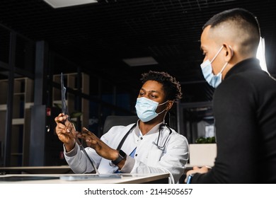 African Doctor Show X-ray Asian Patient. Black Surgeon Analyzing X Ray And Diagnosis Patient In Medical Clinic