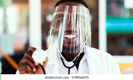 African Doctor Wear Face Shield And Holding Stethoscope With Kind And Smiling.16:9 Style