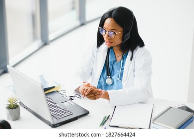 African Doctor Wear Headset Consult Patient Make Online Webcam Video Call On Laptop Screen. Telemedicine Videoconference Remote Computer App Virtual Meeting. Over Shoulder Videocall View.