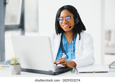 African Doctor Wear Headset Consult Patient Make Online Webcam Video Call On Laptop Screen. Telemedicine Videoconference Remote Computer App Virtual Meeting. Over Shoulder Videocall View.