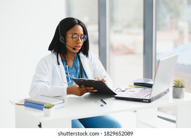 African Doctor Wear Headset Consult Patient Make Online Webcam Video Call On Laptop Screen. Telemedicine Videoconference Remote Computer App Virtual Meeting. Over Shoulder Videocall View.