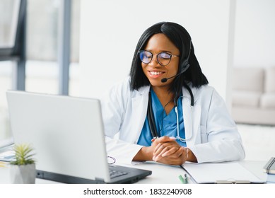 African Doctor Wear Headset Consult Patient Make Online Webcam Video Call On Laptop Screen. Telemedicine Videoconference Remote Computer App Virtual Meeting. Over Shoulder Videocall View.