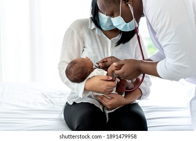 African Doctor Wearing Surgical Mans And Using A Stethoscope, Checking The Respiratory System And Heartbeat Of A 12-day-old Baby Newborn, Who Is Half African Half Thai, To Infant Health Care Concept.