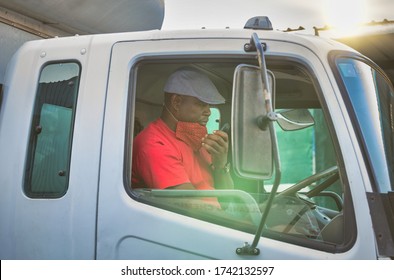 African Driver In The Cabin Of A Truck Talking On The Phone, Wearing A Mask During The Covid Pandemic