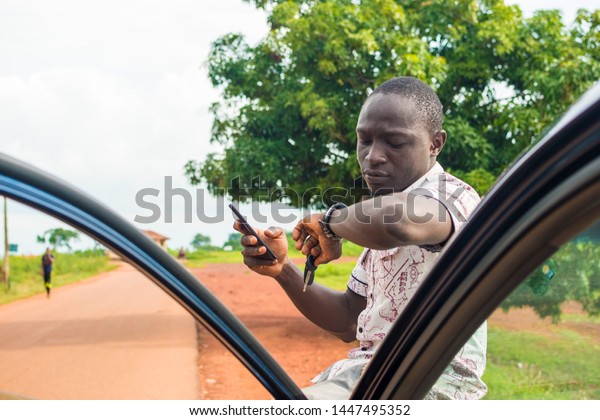 african driver sitting on
the bonnet of his car using his phone but checking his watch as he
waits
