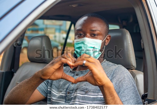 african driver wearing a face mask, doing the heart\
shape with his hands