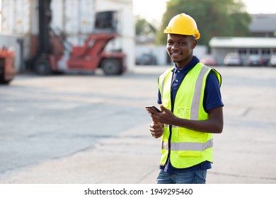 African engineer or factory workers smile and holding smartphone in containers warehouse storage  - Powered by Shutterstock